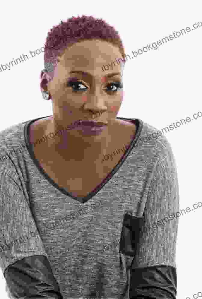 Gina Yashere, A Black Woman With Short Hair And A Big Smile, Is Sitting In A Chair With Her Legs Crossed. She Is Wearing A Black Shirt And Jeans. Cack Handed: A Memoir Gina Yashere